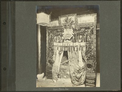 Vertikales, sepiafarbenes Foto eines Himmelbetts mit kunstvoll geschnitztem Holzpfosten und Seidendrapierungen und -bezügen von Unknown